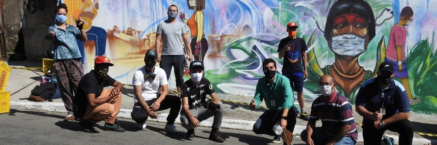 Vários artistas, de máscara, grafitaram em muro em homenagem aos profissionais da saúde, com cores variadas